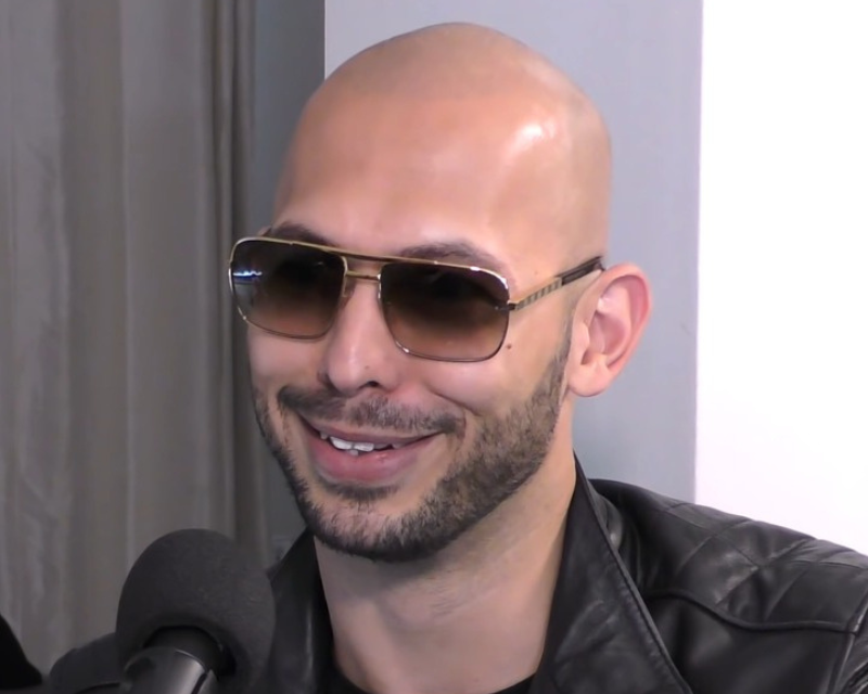 Andrew Tate, wearing sunglasses, sitting in front of a microphone.