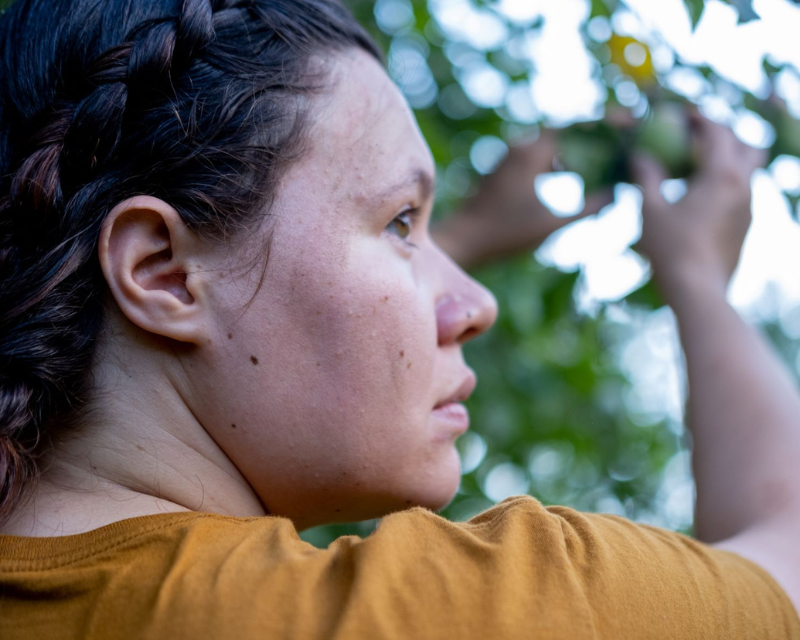 Woman outside picking a fruit from a tree