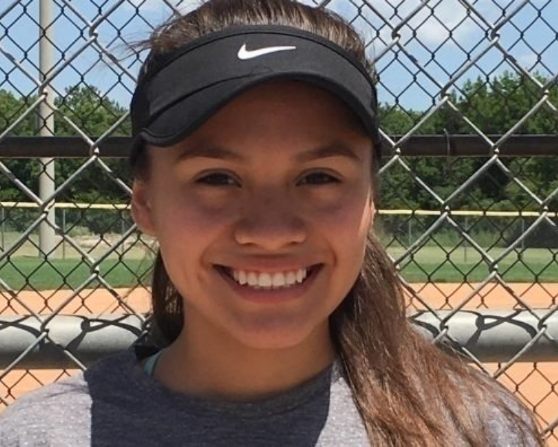 Zephi Trevino, wearing a visor, standing in front of a softball field.